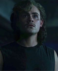 a young man with long hair stares into the distance while standing in a dark room