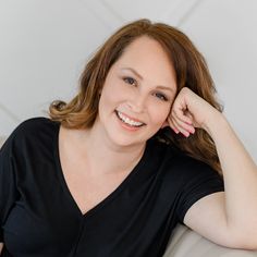 a woman sitting on top of a couch smiling at the camera with her hand on her head