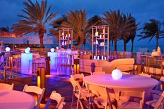 tables and chairs are lit up for an outdoor event with palm trees in the background