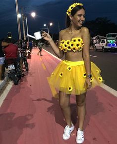 a woman in a sunflower skirt and crop top walking down the street at night