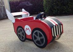 a cardboard race car sitting on top of a cement ground next to bushes and trees