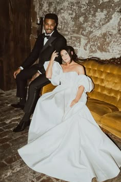 a bride and groom posing for a photo in front of an old couch with gold velvet upholster