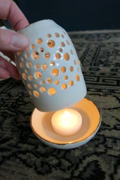 a person is holding a lit candle in a white cup with holes on the inside