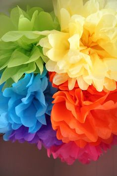 multicolored tissue pom poms hanging from the ceiling in front of a wall