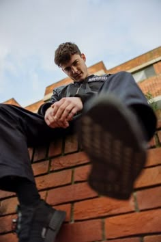 a man sitting on top of a brick wall next to a black shoe with his feet up