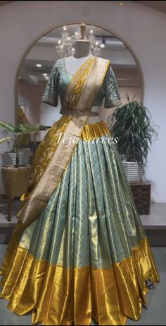 a green and gold dress on display in front of a mirror with a potted plant