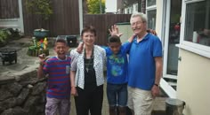 an older man and two young boys standing in front of a house with their hands up