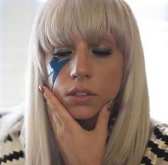 a woman with blond hair and blue eyeliners holding her hand to her face