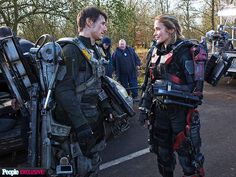 two people dressed as aliens talking to each other in front of some parked cars and motorcycles