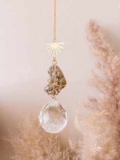 an ornament hanging from a gold chain on top of a tree with feathers