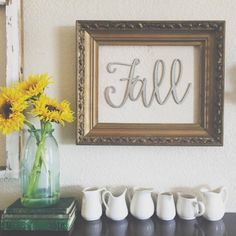 sunflowers are in a vase on a shelf next to a framed sign with the word fall