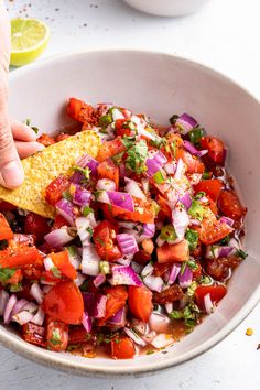 a person dipping a tortilla into a bowl of salsa