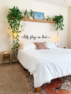 a bed with white sheets and pillows in a bedroom next to a potted plant