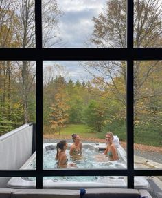 three people are sitting in the hot tub looking out the window at the trees outside