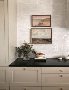 a kitchen with white cabinets and black counter tops is pictured in this image, there are two paintings on the wall