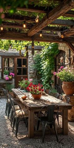 an outdoor dining table with chairs and potted plants on it, under a pergolated roof