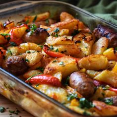 a casserole dish filled with potatoes, peppers and sausage on a wooden table