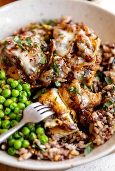 a white bowl filled with rice, peas and meat covered in sauce next to a fork