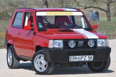 a red and white car parked on top of a gravel road