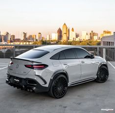 the rear end of a white mercedes suv parked in a parking lot with a city skyline in the background