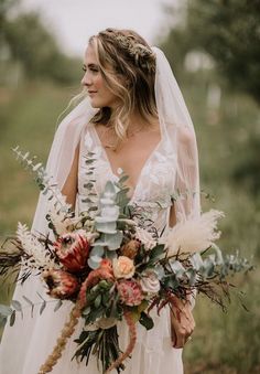 a woman in a wedding dress holding a bridal bouquet with greenery and flowers