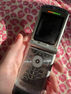 a person holding an old cell phone in their hand on a pink and white blanket