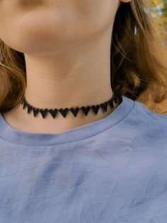 a woman wearing a blue shirt and black beaded choker with hearts on it