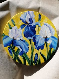 a painting of blue and white flowers painted on a yellow plate with green leaves in the background