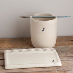 a white ceramic container with a spoon and tray on a wooden table next to it