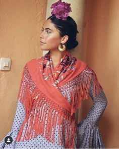 a woman wearing an orange shawl and polka dot dress with pink flowers in her hair