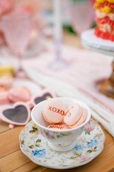 two heart shaped cookies in a teacup on a table next to sunglasses and cake