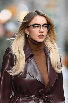 a woman with long blonde hair wearing glasses and a brown leather coat on the street