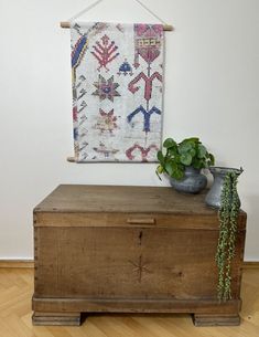 a wooden chest with a potted plant sitting on top of it next to a wall hanging