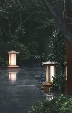 two lanterns lit up in the middle of a walkway with trees and bushes around them