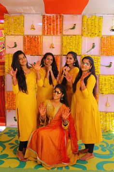 four women in yellow dresses posing for the camera with their hands up and fingers raised