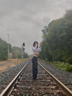 a woman standing on train tracks holding an object in one hand and looking off into the distance