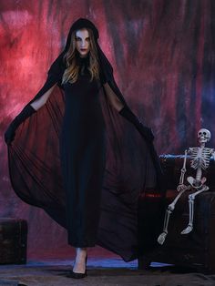 a woman standing in front of a skeleton wearing a long black dress and holding her arms out