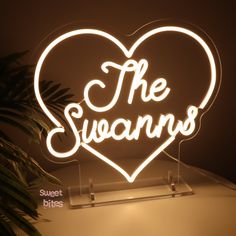 a neon sign that says the swans on top of a table with a plant in front of it