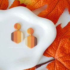 an orange and brown striped earring sitting on top of a white plate next to leaves