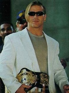 a man in a white jacket and sunglasses holding a wrestling belt