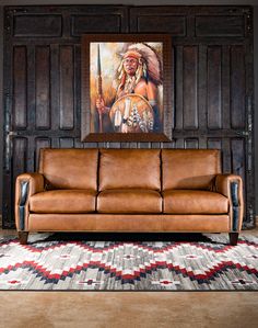 a brown leather couch sitting in front of a wooden paneled wall with a painting on it