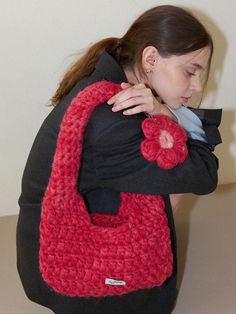 a woman is holding a red crocheted bag with a flower on the front