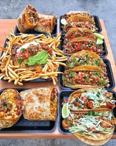 a table topped with trays filled with tacos and burritos covered in toppings