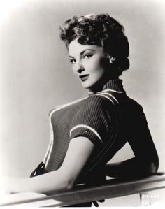 an old black and white photo of a woman leaning on a table with her arms crossed