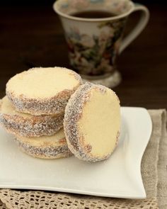 powdered sugar cookies on a plate with a cup of coffee in the background