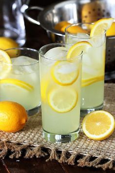 two glasses filled with lemonade sitting on top of a table next to sliced lemons