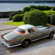 an old car is parked on the side of the road near some bushes and water