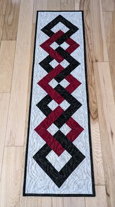 a black, white and red quilted runner on the floor next to a wooden floor