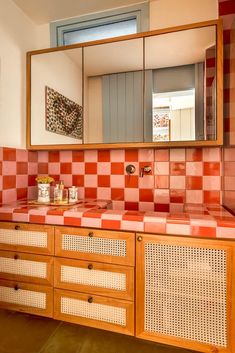 a bathroom with red and white checkered tile on the counter top, mirror above it