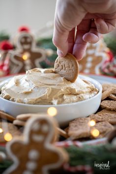 a hand dipping a cracker into a bowl of peanut butter and gingerbread cookies